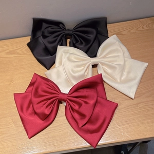 Close-up of three large satin bow hair clips in black, beige and burgundy colors