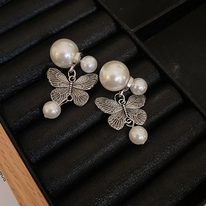 Detailed macro view of vintage butterfly earrings featuring white faux pearls on black velvet
