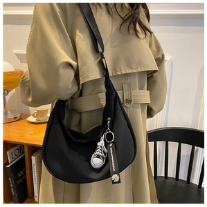 Close-up of black oxford crescent bag with sneaker pendant and floral ribbon detail