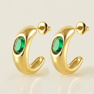 Macro shot of gold C-shaped earrings with inlaid green oval zircon and polished finish