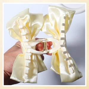 Detail of light yellow satin bow hair claw clip showing the inner plastic grip mechanism