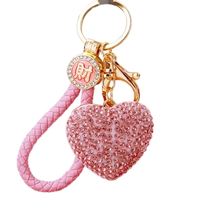 Pink rhinestone heart keychain with gold metal ring and braided leather loop on white background