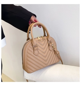 Detail of beige shell handbag showing V-shaped quilted texture and gold metal hardware