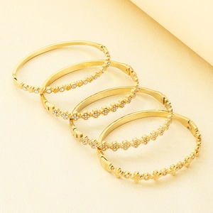 Close-up detail of four gold-plated titanium steel bangles with sparkling cross petal patterns
