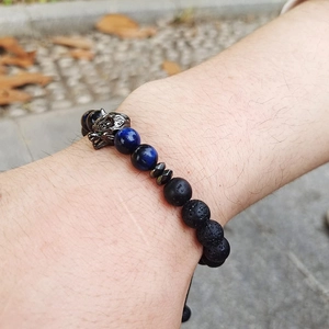 Detail of beaded men's bracelet with black lava stone, blue tiger eye, and wolf head charm