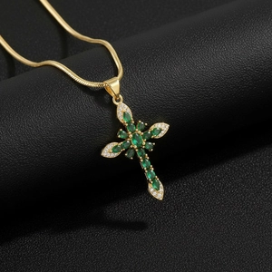 Macro shot of gold cross pendant with green marquise stones on black leather background