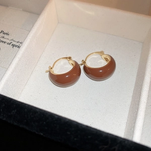 Détail de boucles d'oreilles émaillées marron en forme de C sur un écrin à bijoux texturé