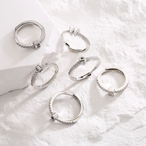 Adjustable silver letter rings with micro-pave cubic zirconia on stone background