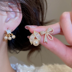 Detail of gold-plated star and pearl earrings with cubic zirconia on a female ear