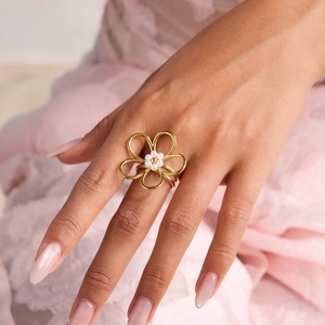 Détail d'une bague fleur dorée avec perles portée sur fond rose doux et élégant