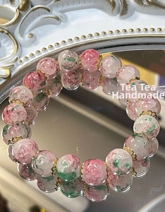 Macro detail of cherry blossom agate beads with gold floral spacers on a mirror surface