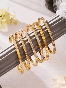 Dettaglio di bracciali dorati con zirconi su un pilastro di pietra e placcatura 18k