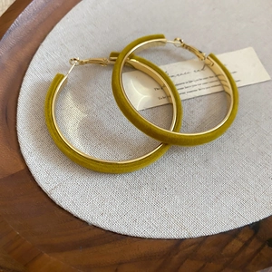 Detail of mustard yellow velvet hoop earrings on beige linen and wooden display tray