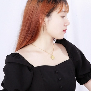Detailed view of a gold zodiac coin necklace worn by a model in a black outfit