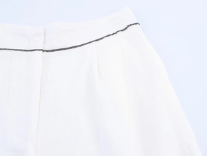 Détail macro du pantalon blanc en coton et lin avec coutures décoratives noires contrastées