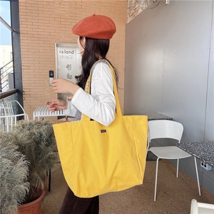 Detail of yellow canvas tote bag with wide strap worn by model against red brick wall