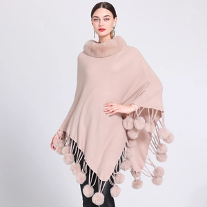 Detail of light pink knitted poncho featuring faux fur collar and pom-pom tassel trim