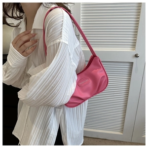 Gros plan sur un sac baguette rose vif porté par un mannequin devant des portes blanches