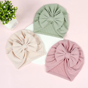 Flat lay of soft ribbed baby turban hats with large bows in pastel green, beige, and pink