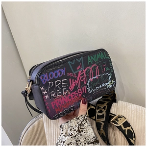 Close-up of black leather camera bag with colorful graffiti prints and wide jacquard strap
