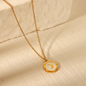 Detail of a gold stainless steel necklace with a moon motif on a beige stone