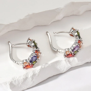 Détail de boucles d'oreilles argentées avec zircons colorés sur fond de roche blanche