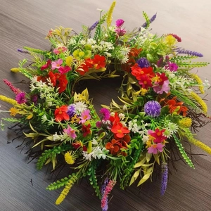 Close-up of vibrant artificial wildflower wreath with green leaves on dark wood background