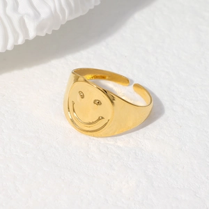 Close-up of a gold-plated stainless steel open ring featuring a smiley face relief design