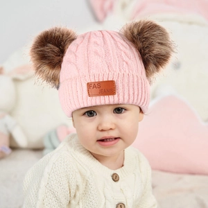 Detailed knit texture of pink baby winter hat with double faux fur pom-poms and leather tag