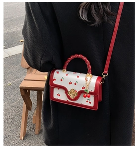 Detail view of a white crossbody bag with cherry prints and golden flower buckle