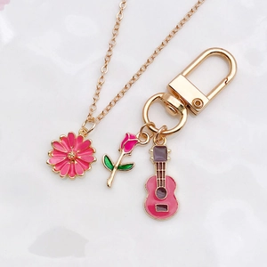 Close-up of pink flower necklace and rose guitar keychain accessories on white surface