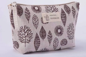 Detail of beige canvas makeup bag with brown leaf pattern and natural style woven label