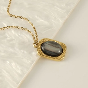 Detailed macro shot of vintage square gold pendant with dark oval gemstone and textured frame