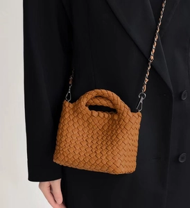 Detail view of woven brown bucket bag featuring braided leather handle and metal chain strap