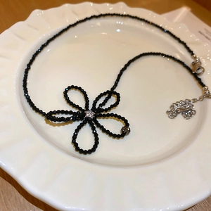 Detail of a black beaded flower necklace with a star centerpiece on a white ceramic plate