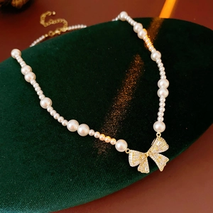 Close-up of pearl necklace with golden bow pendant and sparkling zircon on green velvet