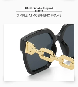 Close-up of black oversized sunglasses frame with decorative gold chain on the temples