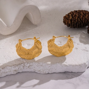 Detailed close-up of golden textured leaf earrings on a minimalist stone display