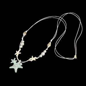 Détail du pendentif étoile de mer avec perles et coquillages sur cordon blanc