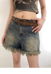 Macro shot of vintage embossed leather belt on distressed blue denim shorts with paint splats