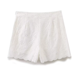 Detail view of white high-waisted shorts with intricate hollow embroidery and wavy hem