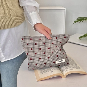 Close-up of a plaid makeup bag with red polka dots and an embroidered bow detail