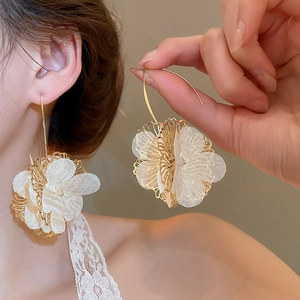 Détail de boucles d'oreilles fleuries avec pétales en fil doré et tissu blanc voilé