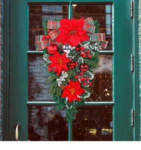Detail of Christmas teardrop wreath with red poinsettias and plaid bow on a green door