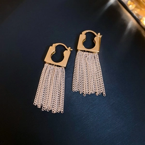 Detail of 14k gold plated square earrings featuring silver tassel chains on blue texture