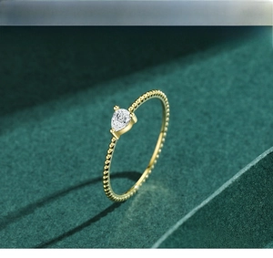 Detail of pear-shaped clear zircon on gold-toned beaded band ring over velvet background