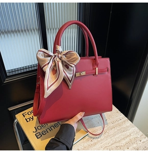 Close-up of red leather handbag featuring gold twist-lock and silk scarf handle detail