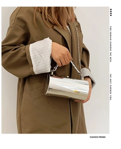 Detail of silver mirror cylinder bag with metallic chain on an olive coat background