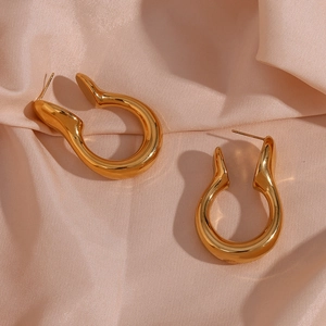 Detailed view of thick golden U-shaped earrings on elegant pink silk background