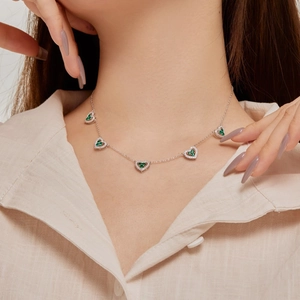Detail of silver necklace with five green heart-shaped zircons worn by a female model